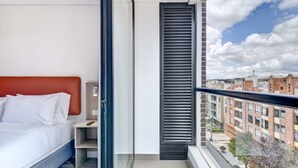 A modern bedroom with a bed, bedside table, and a view of the city through a window. - w* | Heavenly Loft w/ Balcony in Santa Barbara (Bogotá)