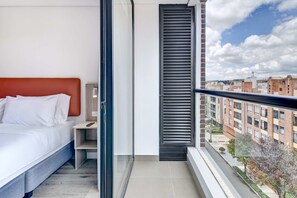 A modern bedroom with a bed, bedside table, and a view of the city through a window. - w* | Heavenly Loft w/ Balcony in Santa Barbara (Bogotá)