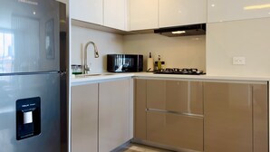 Une cuisine moderne équipée d’un réfrigérateur en acier inoxydable, d’un four à micro-ondes, d’une cuisinière à gaz et de meubles de rangement blancs.