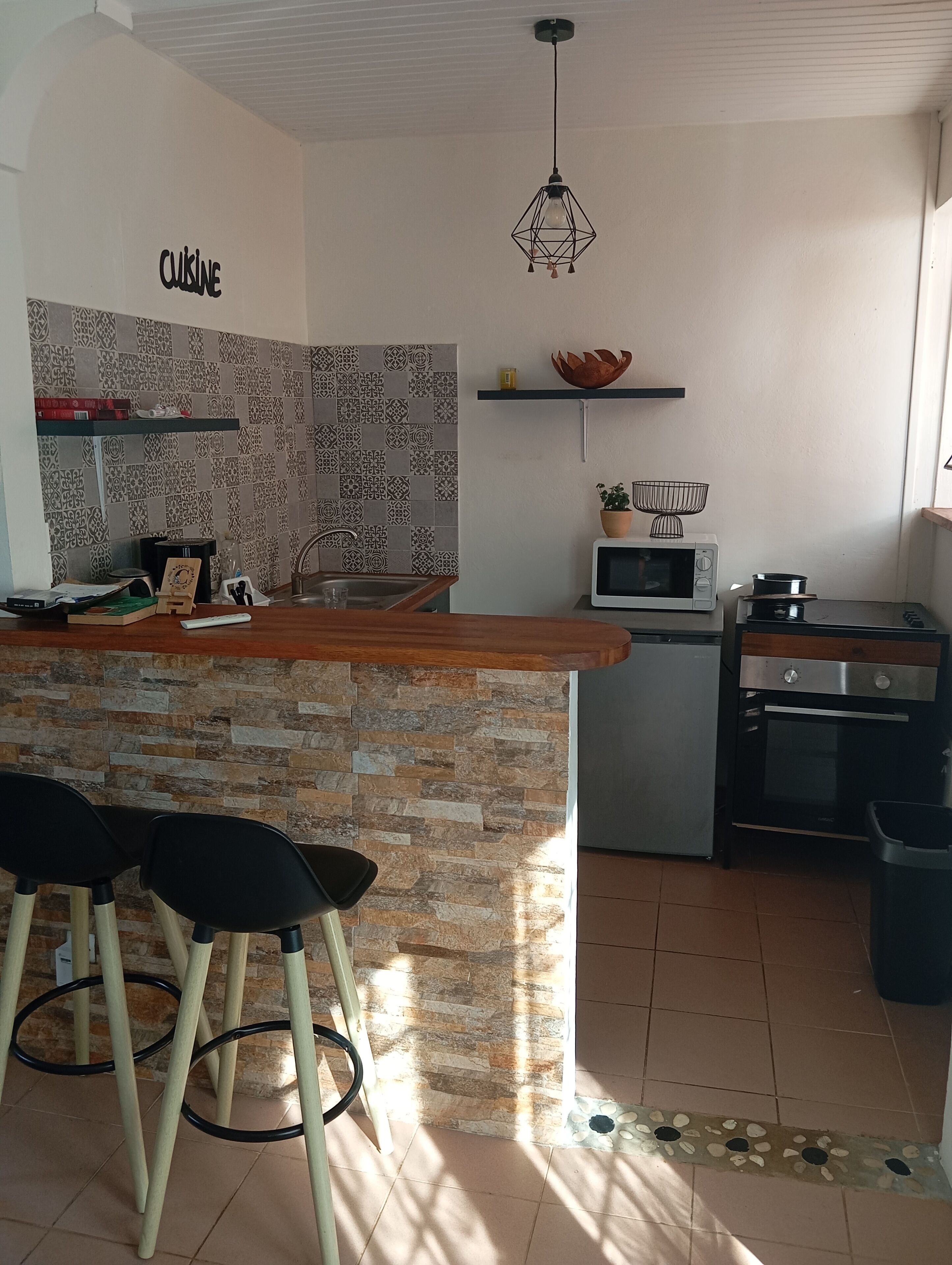 A kitchen with a stone backsplash, a wooden island with bar stools, a microwave, and a stove.