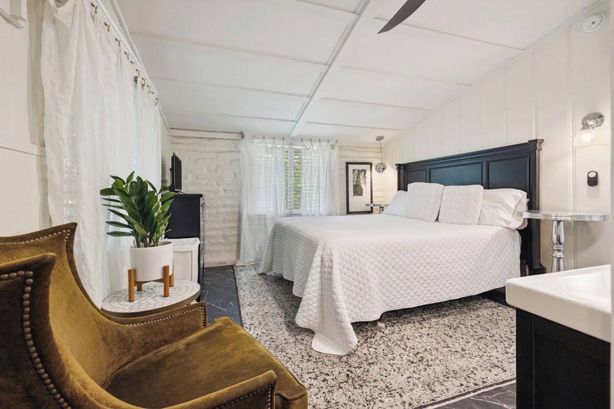 A bedroom with a bed, a chair, a potted plant, a desk, and a bathroom.