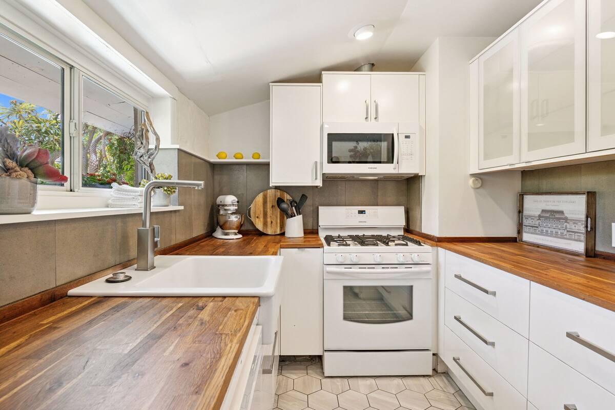 A modern kitchen with white cabinets, a stainless steel sink, a gas stove, and a microwave.