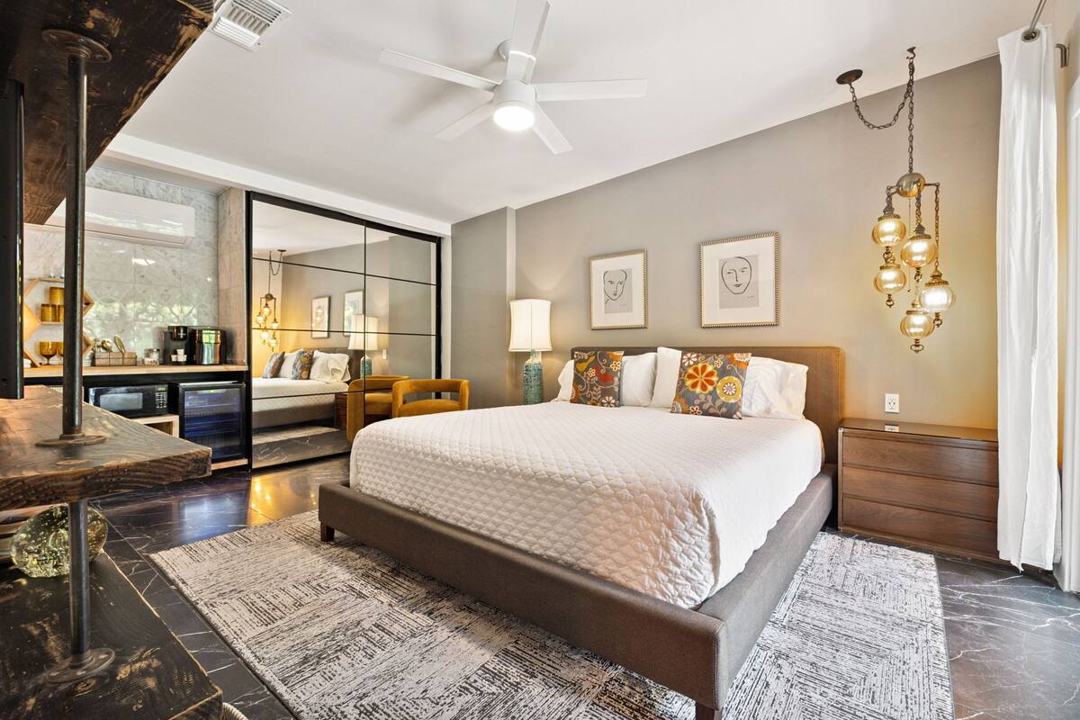 A modern bedroom with a large bed, a ceiling fan, a nightstand, and a bedside table.