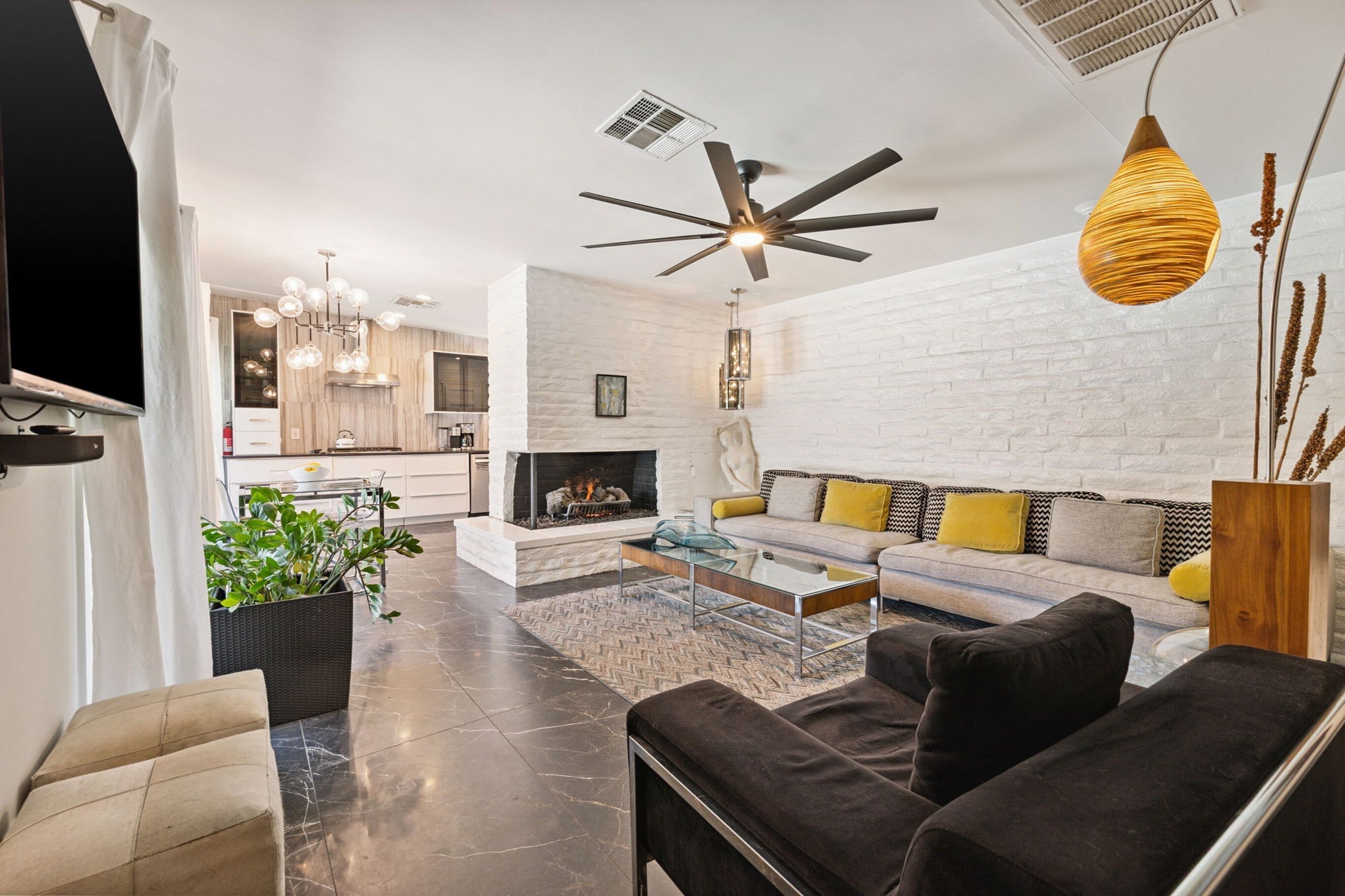 Un salon moderne avec une cheminée, un ventilateur de plafond et un coin repas à l’arrière-plan.