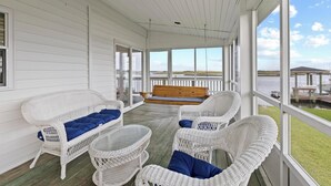 A covered porch with white wicker furniture, a wooden bench, and a view of the water. - Deep Water Access, Best Waterway Views, Pet-Friendly (Surf City)