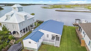 A waterfront property with a large house featuring a blue roof, a covered porch, and a small boat dock. - Deep Water Access, Best Waterway Views, Pet-Friendly (Surf City)