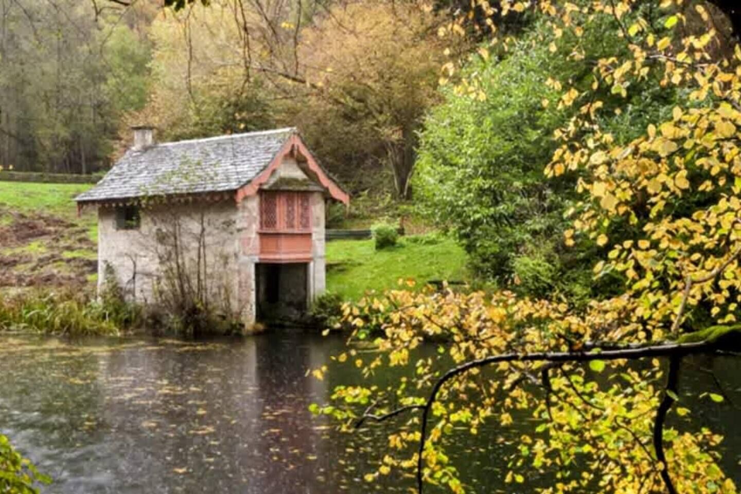 Discover the pretty stone boathouse beside the water among autumn trees.