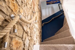 A stone wall with a rope and metal fixtures, a blue carpeted staircase, and a poster on the wall. - Pet-friendly Stonehouse cottage, minutes to the M5 (Gloucestershire)