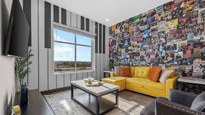 Ein Wohnzimmer mit großem Fenster, einem gelben Sofa, einem Couchtisch und einer Wand voller Poster.