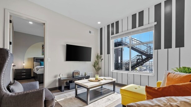 Ein modernes Wohnzimmer mit Flachbildfernseher, Sofa, Couchtisch und Blick auf ein Gebäude mit einer Treppe.