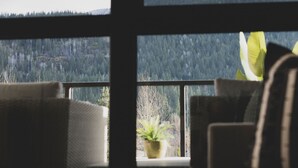 A room with a large window offering a mountain view, a sofa, and a potted plant. - Condo with Mountain Views and Rooftop Hot Tub! (Revelstoke)