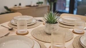 Une table à manger dressée avec des assiettes, des couverts et de la verrerie, agrémentée d’une petite plante en pot et d’un téléviseur en arrière-plan.
