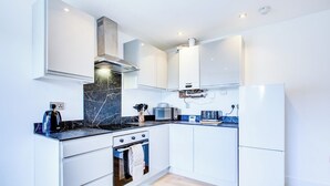 A modern kitchen with white cabinets, a black marble backsplash, a built-in oven, and a microwave. - Superb 4 Bed House with Driveway and Garden (Essex)