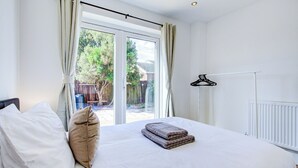 A bedroom with a bed, pillows, a radiator, a window with curtains, and a view of the outside. - Superb 4 Bed House with Driveway and Garden (Essex)