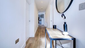 A hallway with a wooden floor, a mirror, and a small table with a vase. - Superb 4 Bed House with Driveway and Garden (Essex)