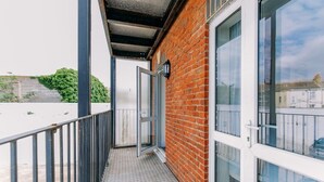 A balcony with a metal railing, a brick wall, and a glass door leading to a room. - Chic 3 Bed Flat on Harbour Way (Kent)