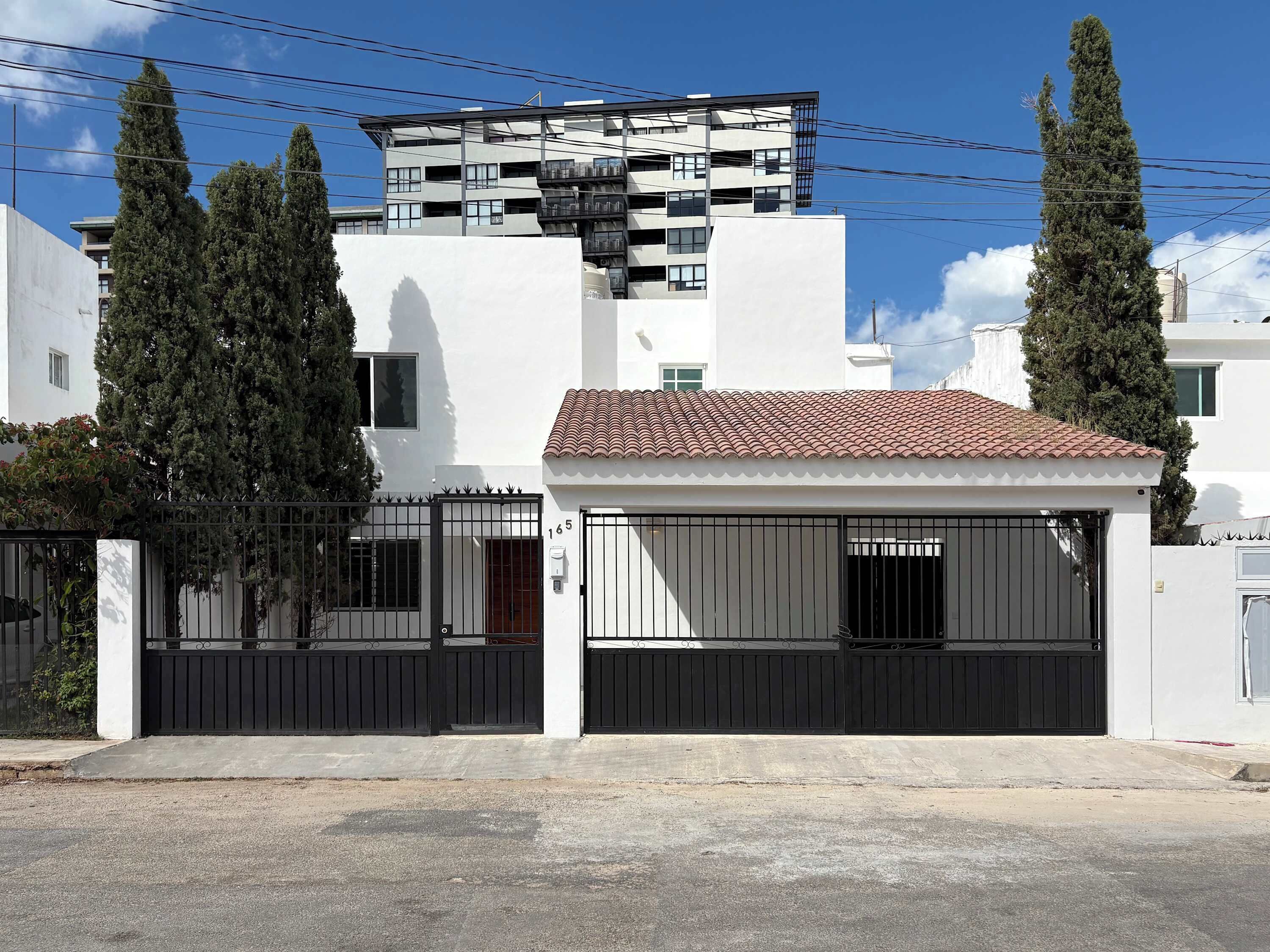 Un immeuble résidentiel moderne avec une façade blanche, un toit recouvert de tuiles rouges et un portail noir.