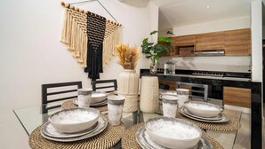 Une cuisine moderne avec des meubles en bois, un plan de travail noir et une table à manger en verre, agrémentée de bols et d’assiettes.