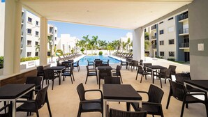 Un espace extérieur avec piscine, comprenant de nombreux chaises longues et tables, entouré de bâtiments dotés de balcons et de palmiers.
