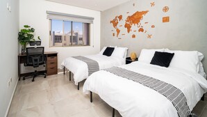 Une chambre d’hôtel avec deux lits, un bureau, une chaise, une plante en pot et une carte du monde accrochée au mur.