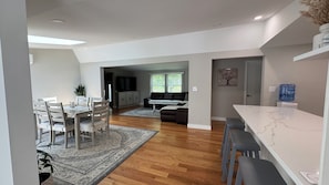 A modern kitchen with wooden flooring, a dining area with a table and chairs, a living room with a sofa and TV, and a water dispenser. - Fantastic 5-bedroom house with a pool in charming Clintondale (Clintondale)
