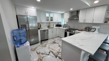 A modern kitchen with white cabinets, stainless steel appliances, and a marble floor.