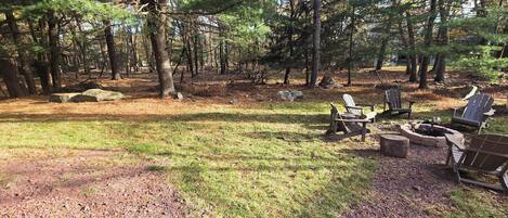 Een bosrijk kampeerterrein met een vuurkuil en Adirondack-stoelen.