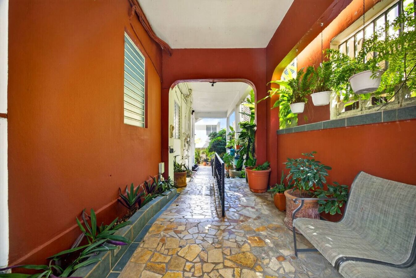 Un couloir étroit, doté d’un sol carrelé, de plantes en pot et d’un banc.