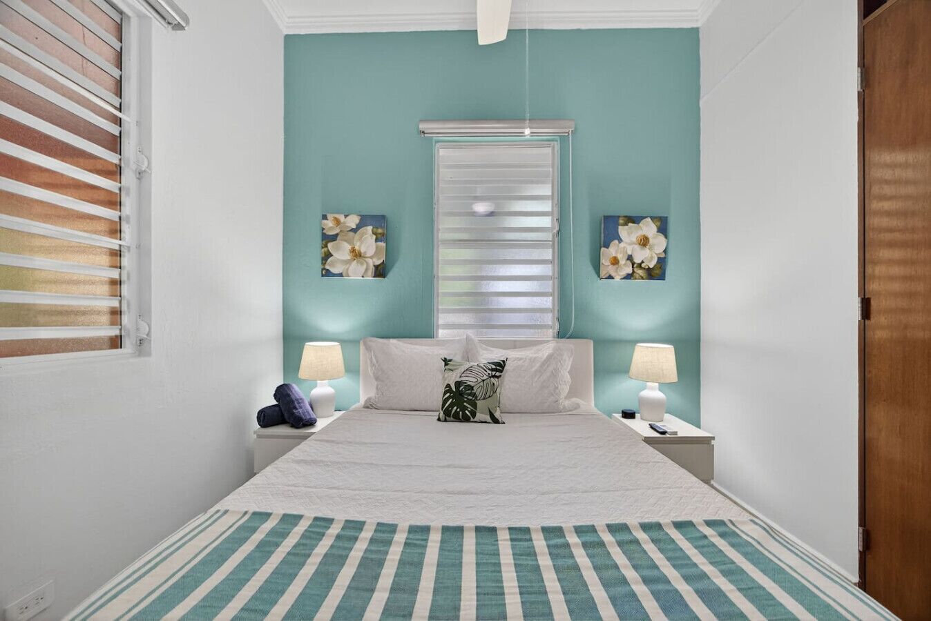 A bedroom with a bed, two nightstands, a window with blinds, and wall art.