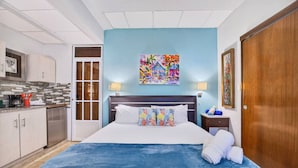 A hotel room with a bed, a nightstand, a painting, a door, and a kitchenette. - Renovated Retreat by Condado Lagoon and Nightlife (San Juan)