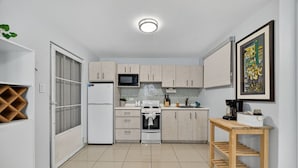 A compact kitchen with a refrigerator, microwave, stove, and sink. There is a wooden table with a tray and a framed picture on the wall. - Spacious Updated Condado Apt Near the Beach (San Juan)