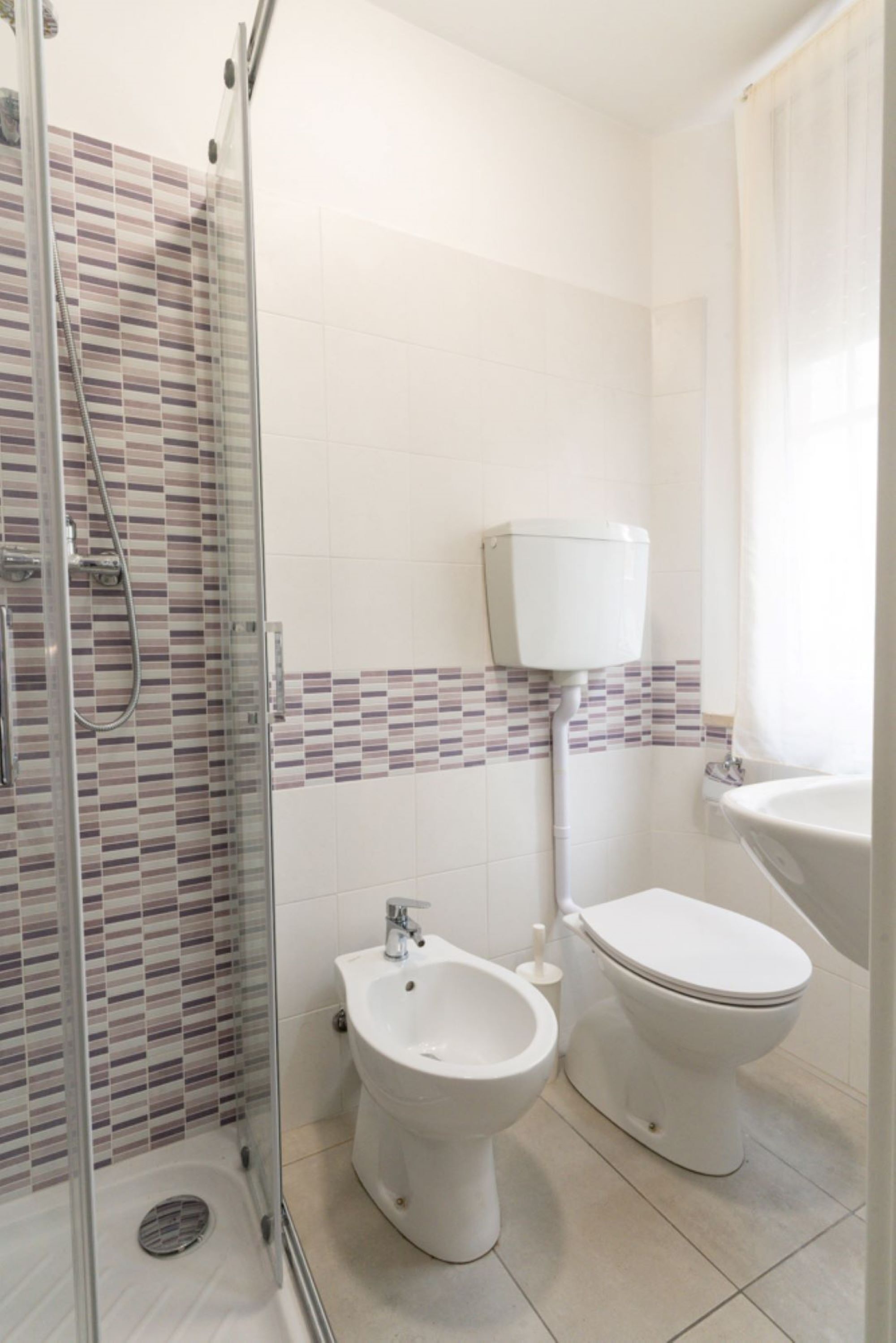 A bathroom with a glass-enclosed shower, a bidet, a toilet, and a sink.
