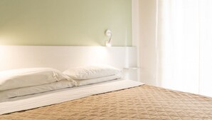 Een net opgemaakt bed met een gewatteerde spreideken, een wit hoofdbord en een nachtkastje met een lamp.