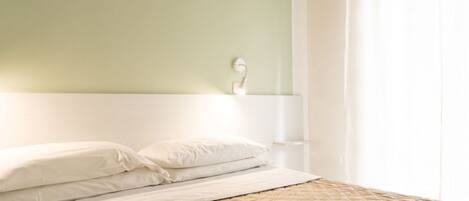 A neatly made bed with a quilted cover, a white headboard, and a bedside table with a lamp.