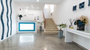 Een moderne receptie met een trap naar de bovenverdiepingen, een receptiebalie en potplanten.