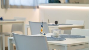 Een moderne eetruimte met witte tafels en stoelen, een decoratief scheepsmodel en een glazen kandelaar.