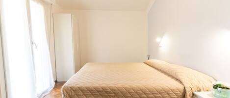 A bedroom with a bed, a nightstand, a dresser, and a window with curtains.