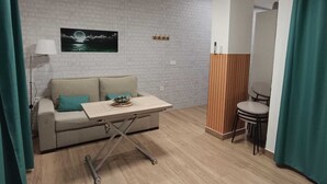 Une pièce moderne avec un mur en briques blanches, un plancher en bois, un canapé agrémenté de coussins turquoise, une petite table, une chaise, une lampe et un luminaire au plafond.