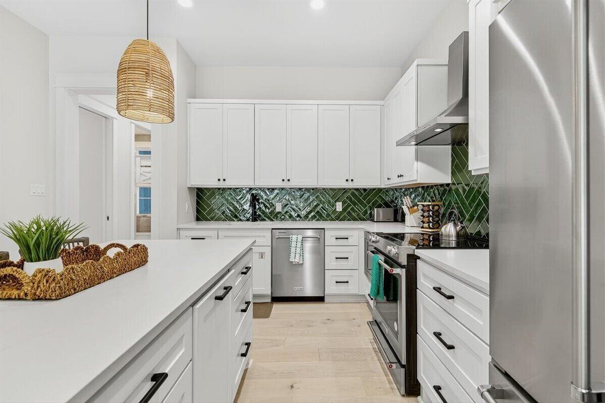 A modern kitchen with white cabinets, a stainless steel refrigerator, and a green tiled backsplash.