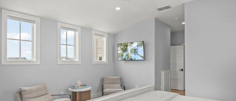 A modern bedroom with a large bed, two chairs, a small table, and a painting on the wall.