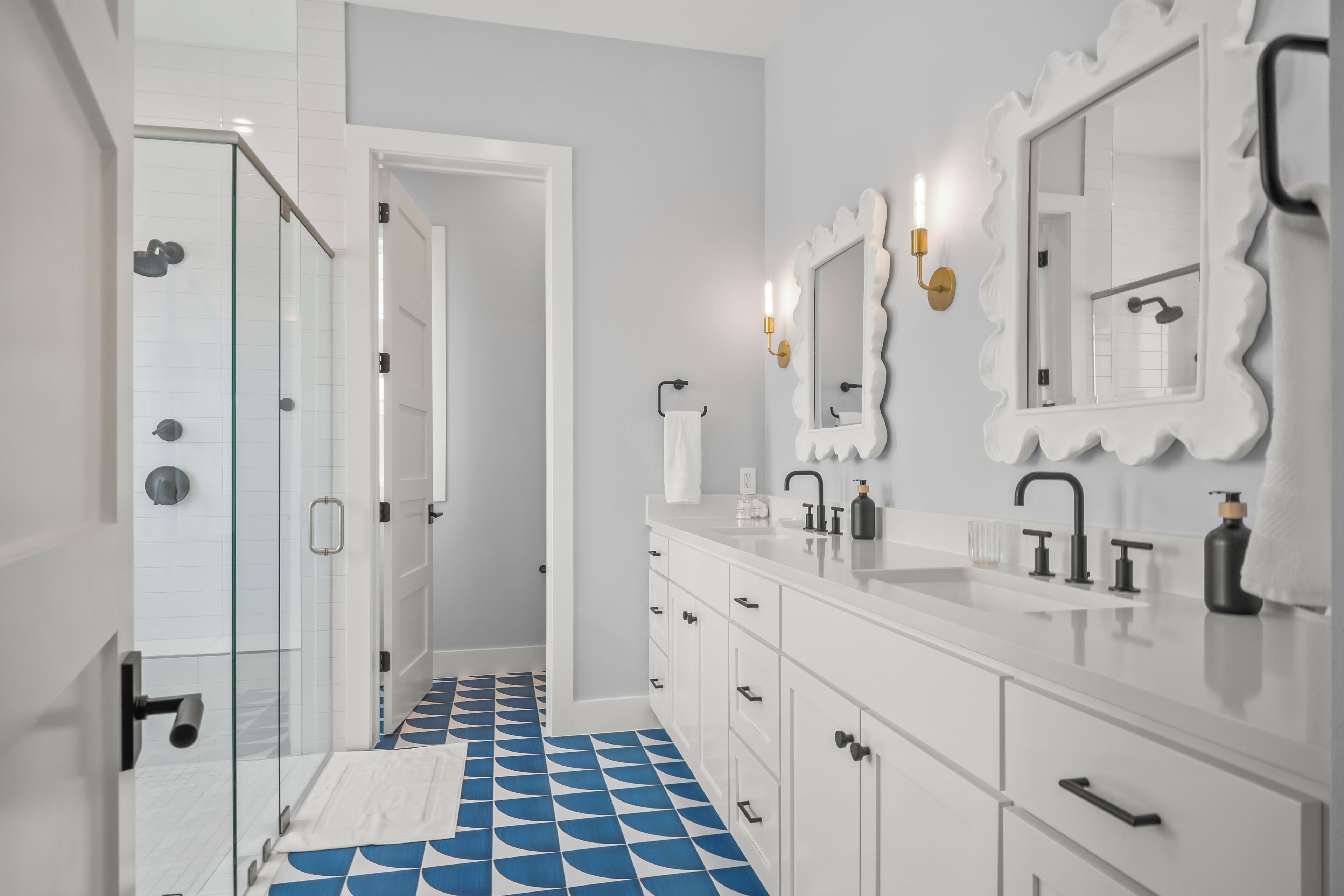 Een moderne badkamer met een douchecabine van glas, witte kastjes en een vloer met blauw-wit patroon.