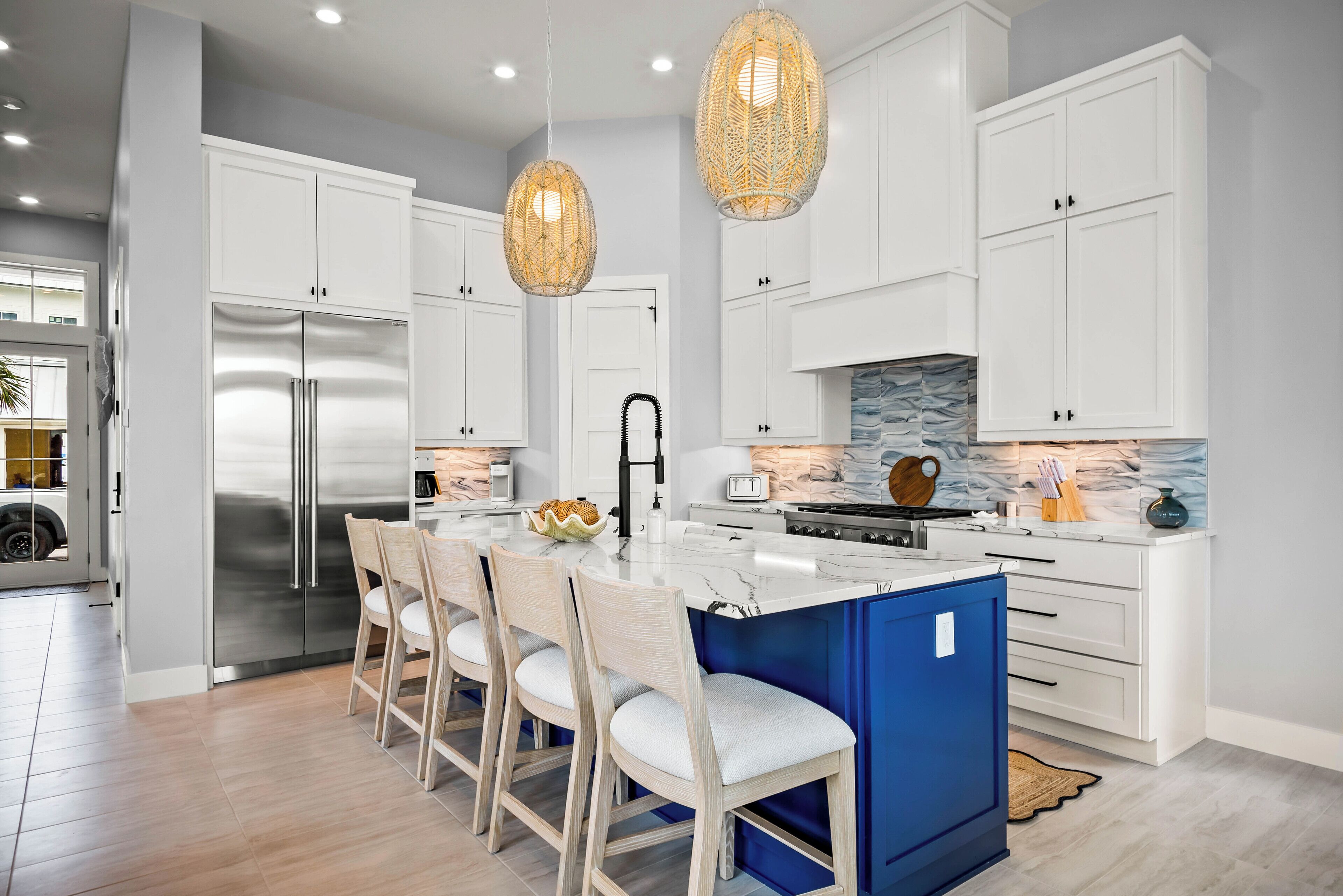 A modern kitchen with white cabinets, a stainless steel refrigerator, a marble island, and a blue accent wall.