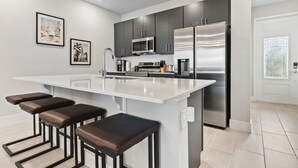 A modern kitchen with a central island, bar stools, stainless steel appliances, and framed artwork on the wall. - Poolside Retreat at Reunion Resort Steps from the Water & Minutes to Disney (Kissimmee)