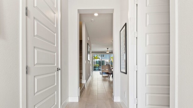 A hallway with white doors and a tiled floor leading to a dining area with a table and chairs. - Poolside Retreat at Reunion Resort Steps from the Water & Minutes to Disney (Kissimmee)