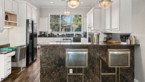 A modern kitchen with white cabinetry, granite countertops, and a central island with bar stools. - New! EPIC Playhouse- Theater, Bunks, Pool & Arcade (Kissimmee)