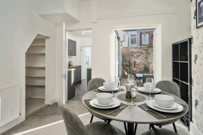 A dining area with a round table set for four, a kitchen in the background, and a view of the outside. - Home for 5 | Free Parking | All Amenities (Redcar and Cleveland)