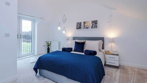 Quarto com cama, mesas de cabeceira, obras de arte na parede e vista através de uma porta.