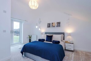 Ein Schlafzimmer mit Bett, Nachttischen, Wandbildern und Blick durch eine Tür.