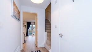 Um corredor com um radiador, um tapete listrado, uma escada e uma porta que dá para um quarto com janela.