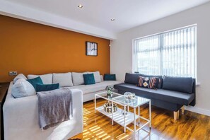 A modern living room with a white sofa, a dark sofa, and a glass coffee table.